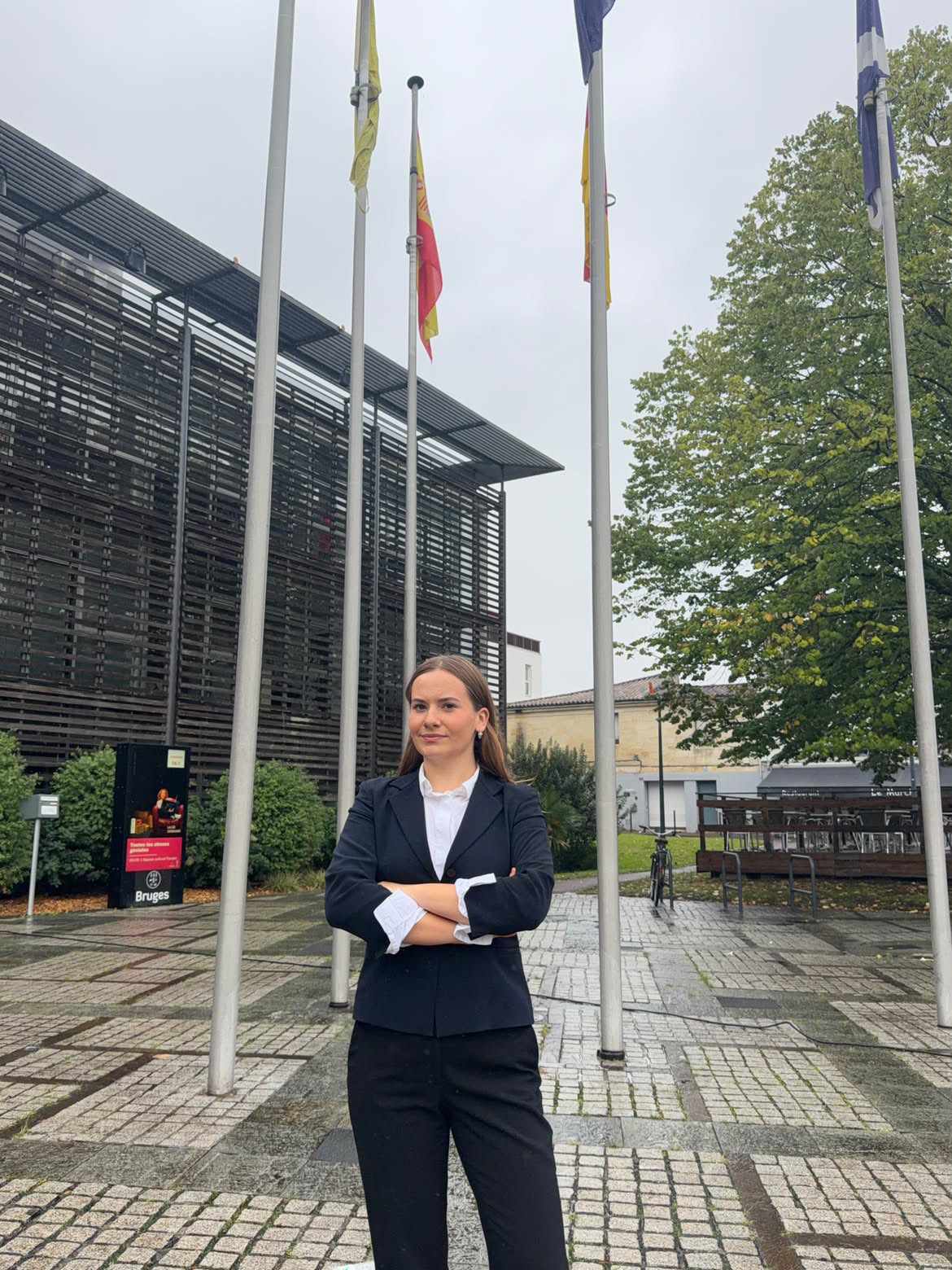 Clara Caurier debout sur un parvis, devant un bâtiment et des mâts de drapeaux